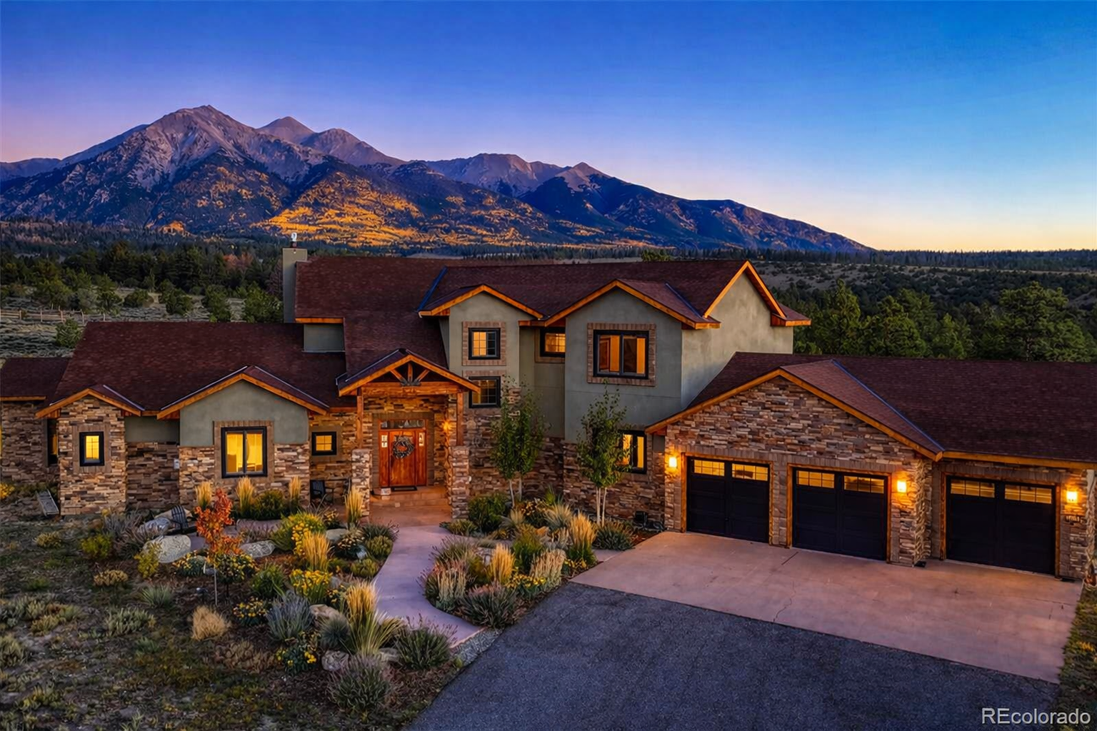 Stone and timber mountain home at dusk with the Sawatch Range glowing behind it