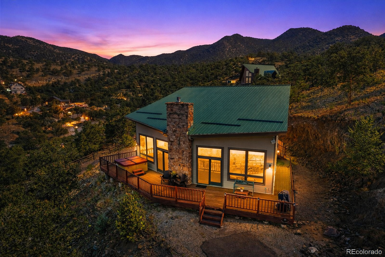 Hillside mountain home with a wraparound deck glowing at dusk under a purple Colorado sky